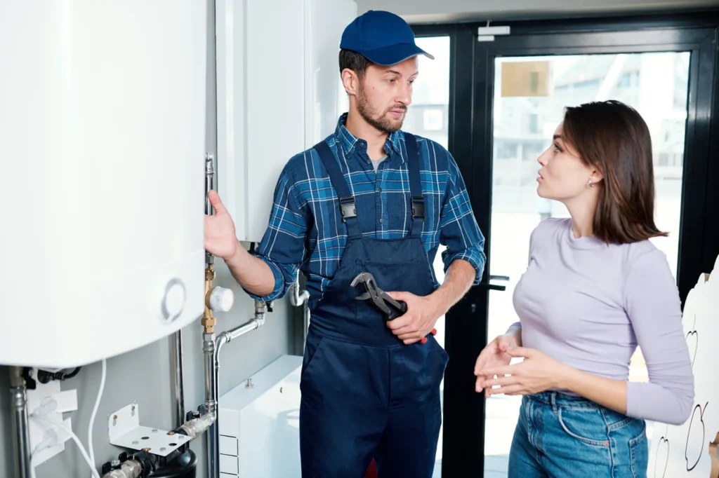 Plumber repairing a home water heater while the homeowner looks on