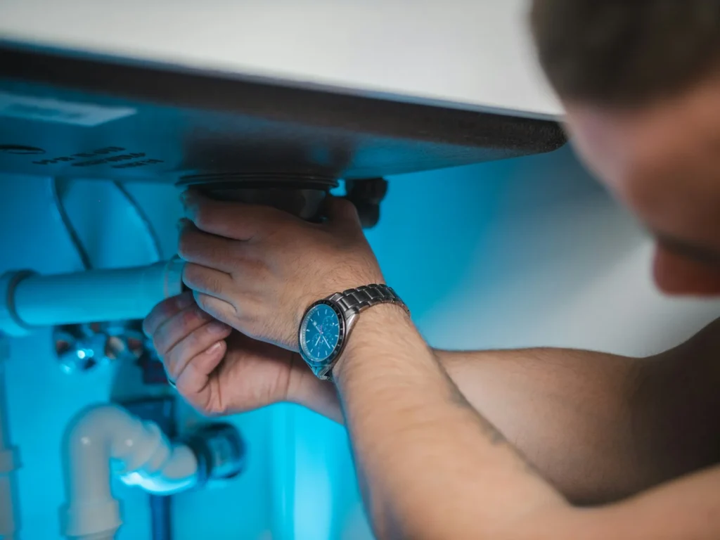 Plumber's hands checking the pipe connections inside a sink cabinet