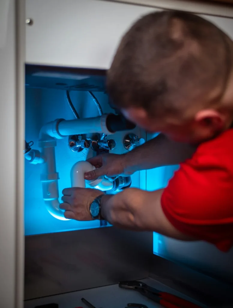 Plumber working on the drain trap inside a sink cabinet